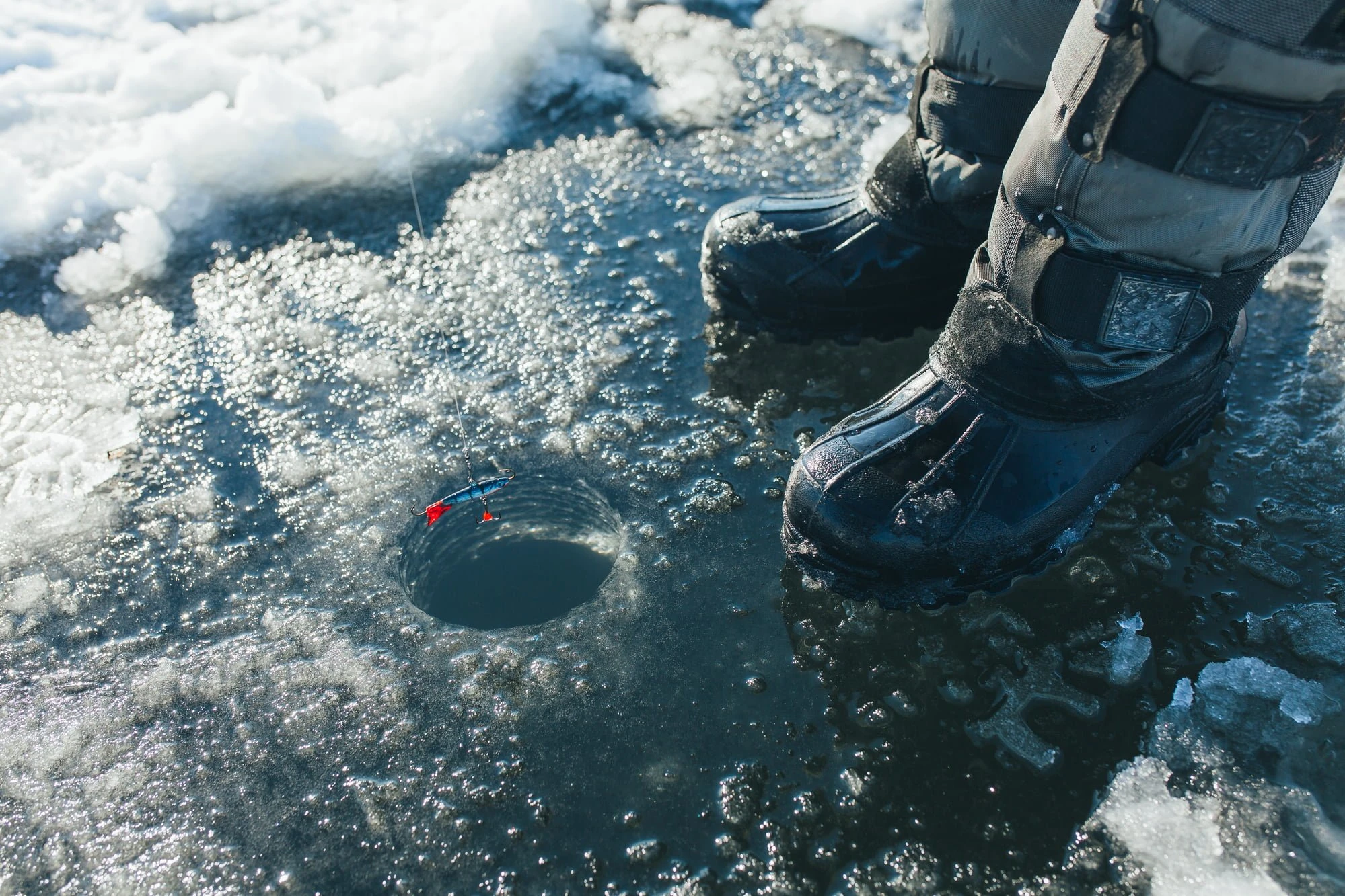 person standing on ice with hole drilled for ice fishing